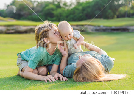 Mother, older son, and newborn baby on a meadow in the park. Family spending quality time together in nature. Parenthood, love, and family bond concept Mother, older son, and newborn baby on a meadow in the park. Family spending quality time together in nature. Parenthood, love, and family bond concept 130199151