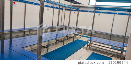 Minimalist sports changing room with blue benches, numbered hooks, and drainage mats. Concept for an organized changing area in a modern fitness club or swimming pool. 130199344