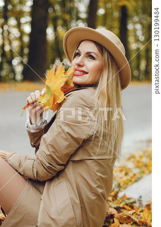 Woman posing for a photo in the autumn park. Caucasian girl has red lips. Woman wearing beige coat and a hat. Woman posing for a photo in the autumn park. Caucasian girl has red lips. Woman wearing beige coat and a hat. 130199484