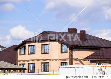 Decorative metal on the roof of a brick house. Fence made of corrugated metal. Decorative metal on the roof of a brick house. Fence made of corrugated metal. 130199596