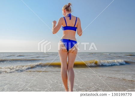 Woman in a blue swimsuit by the sea. A palm print in the form of sand on the priest at the woman 130199770