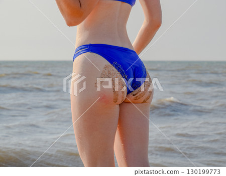 Woman in a blue swimsuit by the sea. A palm print in the form of sand on the priest at the woman 130199773