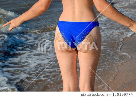 Woman in a blue swimsuit by the sea. A palm print in the form of sand on the priest at the woman 130199774