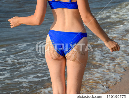 Woman in a blue swimsuit by the sea. A palm print in the form of sand on the priest at the woman 130199775