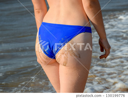 Woman in a blue swimsuit by the sea. A palm print in the form of sand on the priest at the woman 130199776