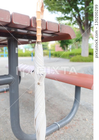 A white umbrella forgotten on a park bench 130200299
