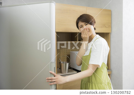 A woman in an apron opening a refrigerator 130200782