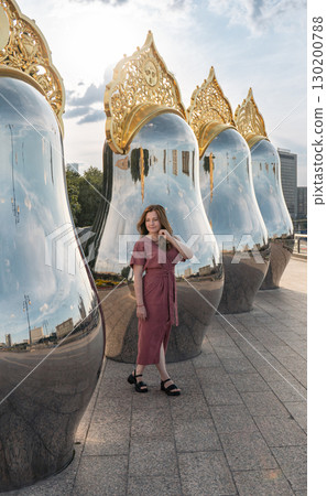Woman in a dusty rose dress poses beside large reflective sculptures with ornate golden tops in Moscow 130200788