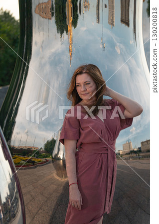 Woman in a rose dress poses beside giant reflective matryoshka sculptures with golden tops on Taras Shevchenko Embankment in Moscow Woman in a rose dress poses beside giant reflective matryoshka sculptures with golden tops on Taras Shevchenko Embankment in Moscow 130200818