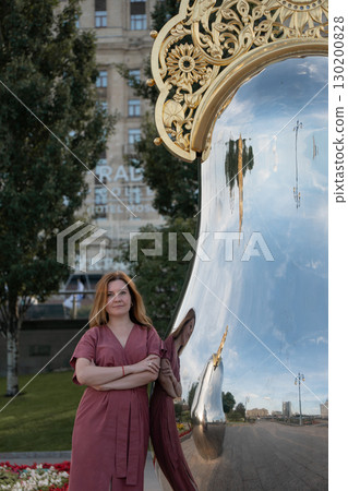 Woman in rose dress stands by a mirrored art installation with golden ornament near Radisson Hotel Woman in rose dress stands by a mirrored art installation with golden ornament near Radisson Hotel 130200828