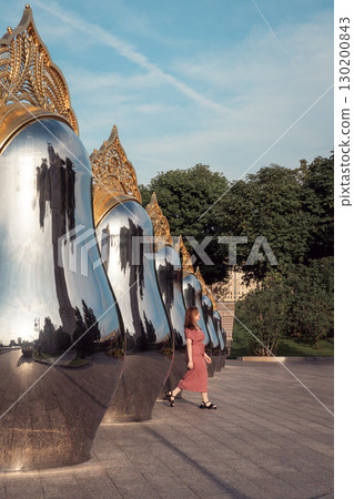 Woman in a rose dress walking along the Matryoshka sculpture installation on Taras Shevchenko Embankment in Moscow Woman in a rose dress walking along the Matryoshka sculpture installation on Taras Shevchenko Embankment in Moscow 130200843