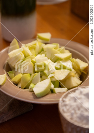 Freshly chopped green apples in a beige plate on a wooden table, prepared for baking 130200895