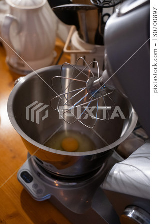 Fresh egg in a stainless steel mixing bowl of an electric stand mixer, ready for whisking on a wooden kitchen counter Fresh egg in a stainless steel mixing bowl of an electric stand mixer, ready for whisking on a wooden kitchen counter 130200897