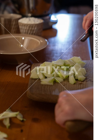 Freshly chopped green apple pieces are transferred from a wooden cutting board into a bowl, with a cup of flour visible in the background Freshly chopped green apple pieces are transferred from a wooden cutting board into a bowl, with a cup of flour visible in the background 130200898