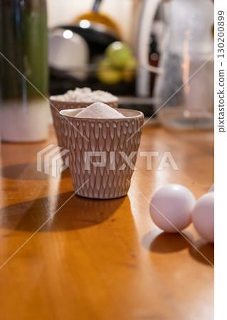 White eggs, sugar, and flour in decorative ceramic cups on a wooden kitchen counter, prepared for baking White eggs, sugar, and flour in decorative ceramic cups on a wooden kitchen counter, prepared for baking 130200899
