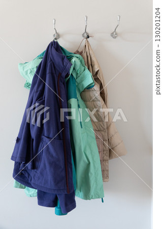 Simple interior view with colorful jackets and coats hanging on metal wall hooks against a plain white background 130201204