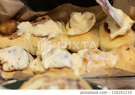 Woman spreading tasty cream onto baked cinnamon rolls on table in kitchen 130201210