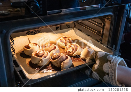 Woman taking tray with fresh cinnamon rolls from electric oven Woman taking tray with fresh cinnamon rolls from electric oven 130201238