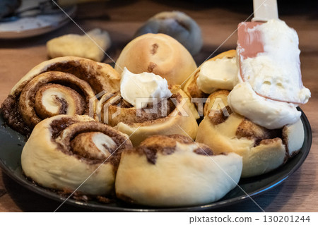 Woman spreading tasty cream onto baked cinnamon rolls on table in kitchen 130201244