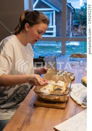 Woman spreading tasty cream onto baked cinnamon rolls on table in kitchen Woman spreading tasty cream onto baked cinnamon rolls on table in kitchen 130201255
