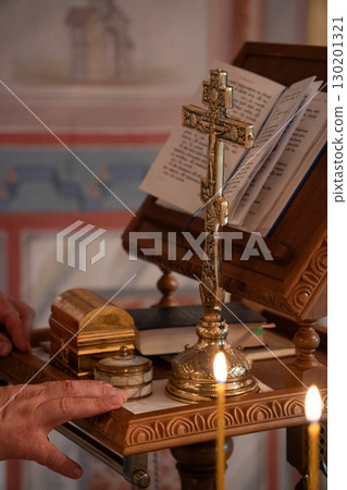 Orthodox cross standing on a carved wooden altar next to a golden box, marble container, and an open liturgical book, with candles burning in front Orthodox cross standing on a carved wooden altar next to a golden box, marble container, and an open liturgical book, with candles burning in front 130201321
