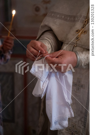 Close-up of an Orthodox priest preparing a white christening garment during a baptism ceremony Close-up of an Orthodox priest preparing a white christening garment during a baptism ceremony 130201328