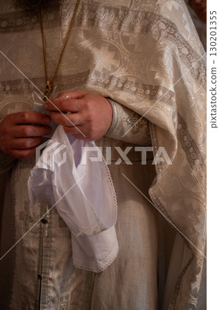 Close-up of an Orthodox priest preparing a white christening garment during a baptism ceremony 130201355