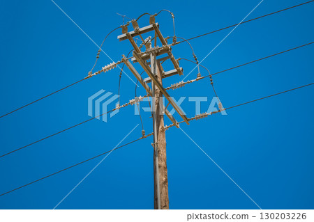 Power line pole with overhead wires for electricity transmission above ground against clear blue sky 130203226
