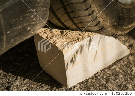 Huge stone blocks car wheel during emergency tire change on road Huge stone blocks car wheel during emergency tire change on road 130203290