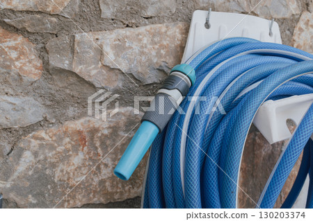 Garden hose with spray nozzle on holder by stone wall 130203374