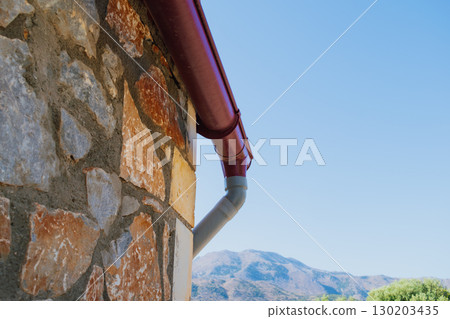Rainwater drainage system of a building near a stone wall, designed to collect and divert precipitation from the roof 130203435