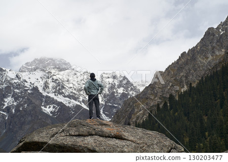 asian man standing on top of rock looking at peak of snow mountain asian man standing on top of rock looking at peak of snow mountain 130203477