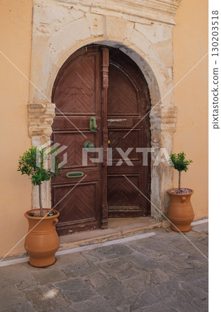Antique massive wooden door with arched opening and wrought iron elements, Star of David. Mediterranean style. Small olive trees in clay pots near the door for coziness Antique massive wooden door with arched opening and wrought iron elements, Star of David. Mediterranean style. Small olive trees in clay pots near the door for coziness 130203518