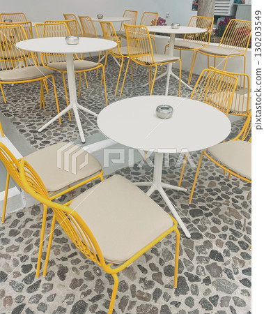 Cozy cafe in an unusual Santorini style with yellow metal chairs and white round tables 130203549