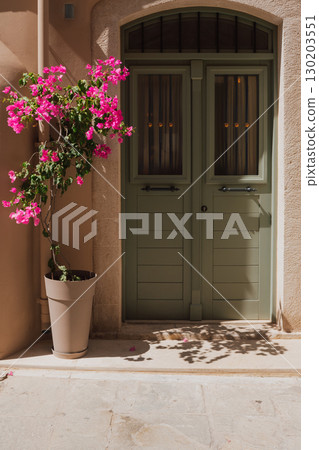 Cozy entrance area, luxurious bougainvillea in a flower pot near the olive colored front door, Mediterranean style of the old town of Rethymno 130203551