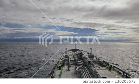 View from ship stern moving through the sea. Large tanker in the background under cloudy sky View from ship stern moving through the sea. Large tanker in the background under cloudy sky 130203572