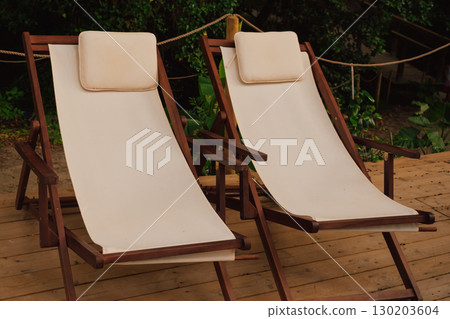 Comfortable lounge chairs with white cushions located in a forest recreation area for enjoying beauty and fresh air 130203604
