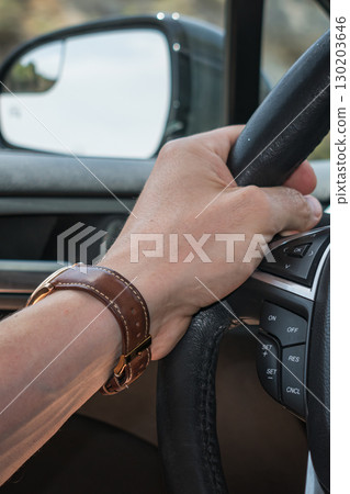 Male hand with watch and brown strap holding a car steering wheel Male hand with watch and brown strap holding a car steering wheel 130203646