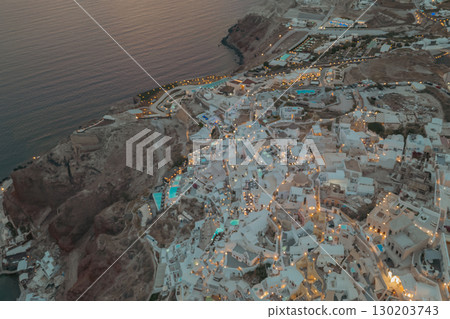 Oia, Santorini, Greece. Evening drone view with warm street lights illuminating the white houses Oia, Santorini, Greece. Evening drone view with warm street lights illuminating the white houses 130203743