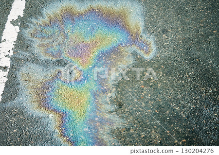 Gasoline or oil spill creating rainbow sheen on asphalt road surface. 130204276