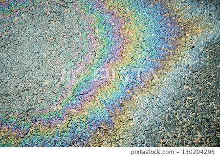 Rainbow oil slick on asphalt road creates colorful abstract pattern, highlighting environmental pollution. 130204295