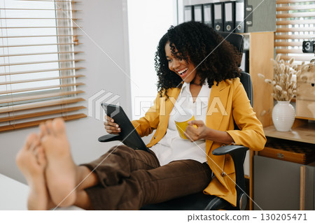 Businesswoman enjoying a coffee break in a modern office, using a tablet, relaxing Businesswoman enjoying a coffee break in a modern office, using a tablet, relaxing 130205471