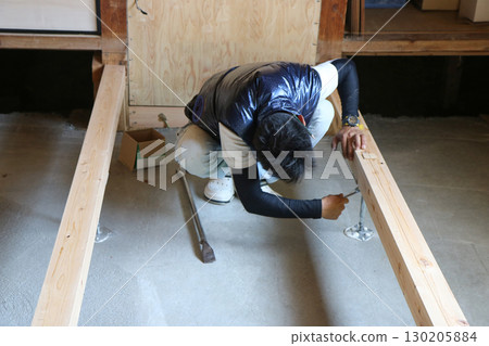 A carpenter is adjusting the steel beams between the concrete floor and the joists. A carpenter is adjusting the steel beams between the concrete floor and the joists. 130205884