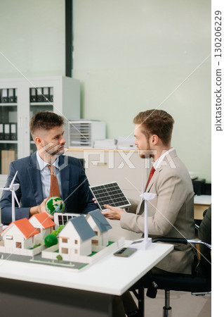 Experts collaborate on renewable energy solutions with house models, wind turbines, and solar panels, 130206229