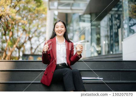 Confident Asian woman with a smile standing holding notepad and tablet at out side office. Confident Asian woman with a smile standing holding notepad and tablet at out side office. 130207070