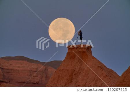 A photographer captures the full moon over a serene desert at dusk 130207315