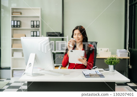 Asian woman using laptop and tablet while sitting at her working place 130207401