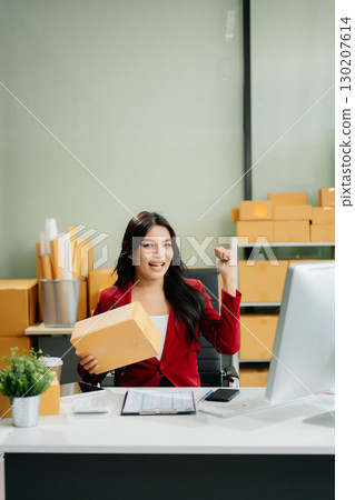 Asian woman prepares parcels and checks online orders on tablet and laptop for delivery online shopping 130207614