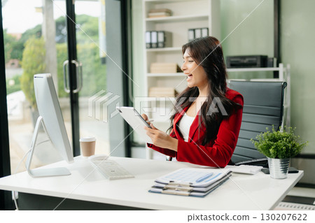 Asian woman using laptop and tablet while sitting at her working place 130207622