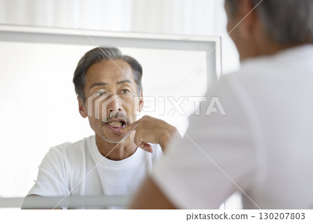 A man in his 60s who looks in the mirror and worries about his gums 130207803
